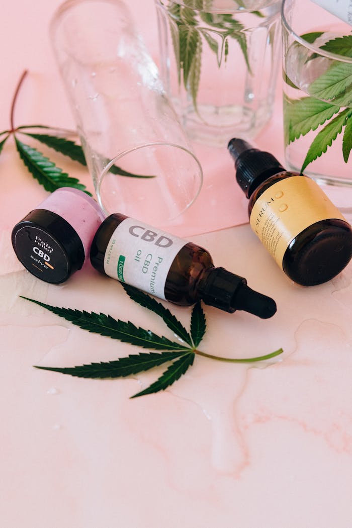 heros-img Aesthetic arrangement of CBD oil bottles with cannabis leaves on a pink background.